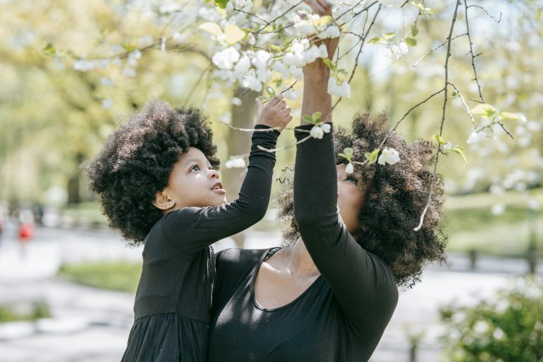 Mother holds her daughter as they both lovingly look up at flowers in a tree